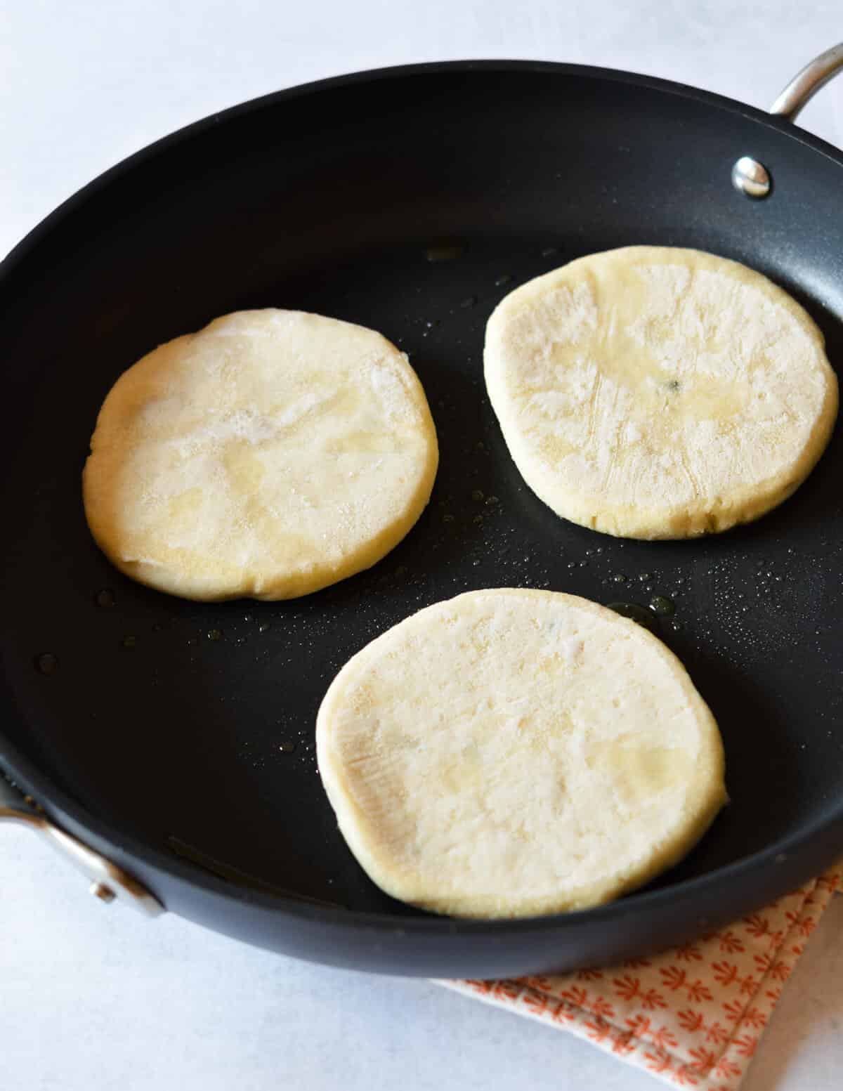 three frozen pupusas in a skillet. 