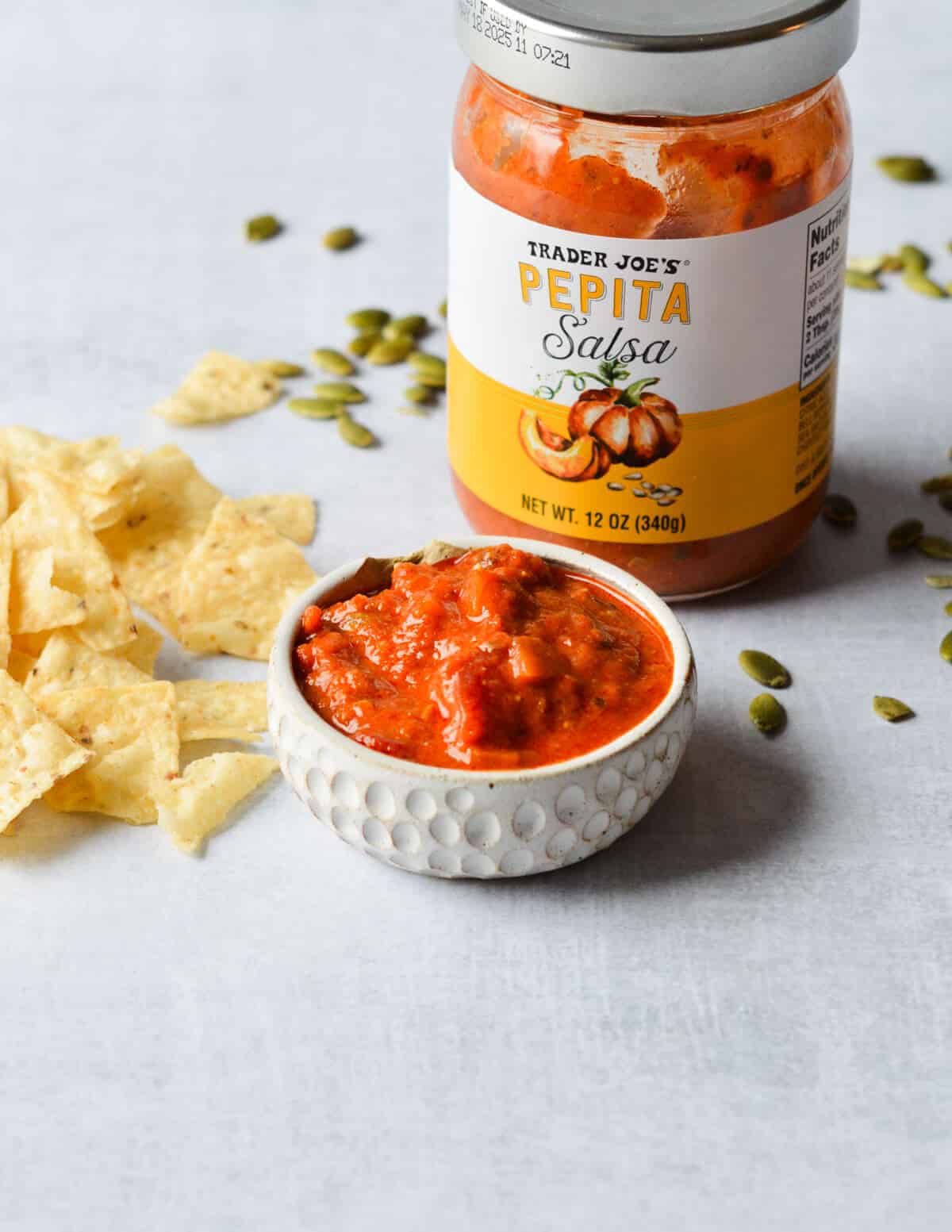 a small bowl of pepita salsa next to chips and a jar of salsa. 